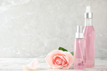Bottles Of Essential Oil And Rose On Marble Table. Space For Text