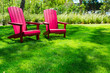 © MichaelVi - Traditional curveback sunset red plastic outdoor patio adirondack chairs with contoured backs and seats on green grass of outdoor lawn. Design, concept, idea