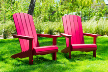 Traditional Curveback Sunset Red Plastic Outdoor Patio Adirondack Chairs With Contoured Backs And Seats On Green Grass Of Outdoor Lawn. Design, Concept, Idea