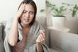 © sorrapongs - Asian Cute of  girl having headache and high temperature from illness holding pill of medicine sitting on sofa at home, Health and illness concepts