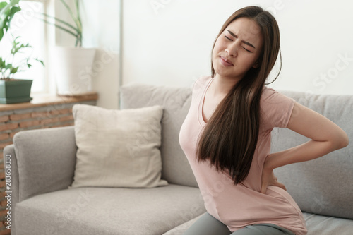 Cuadros en Lienzo Asian girl having Waist pain sitting on sofa at home