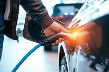 Human hand is holding Electric Car Charging connect to Electric car