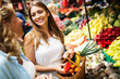 © NDABCREATIVITY - Young women friends baying vegetables and fruits on the market