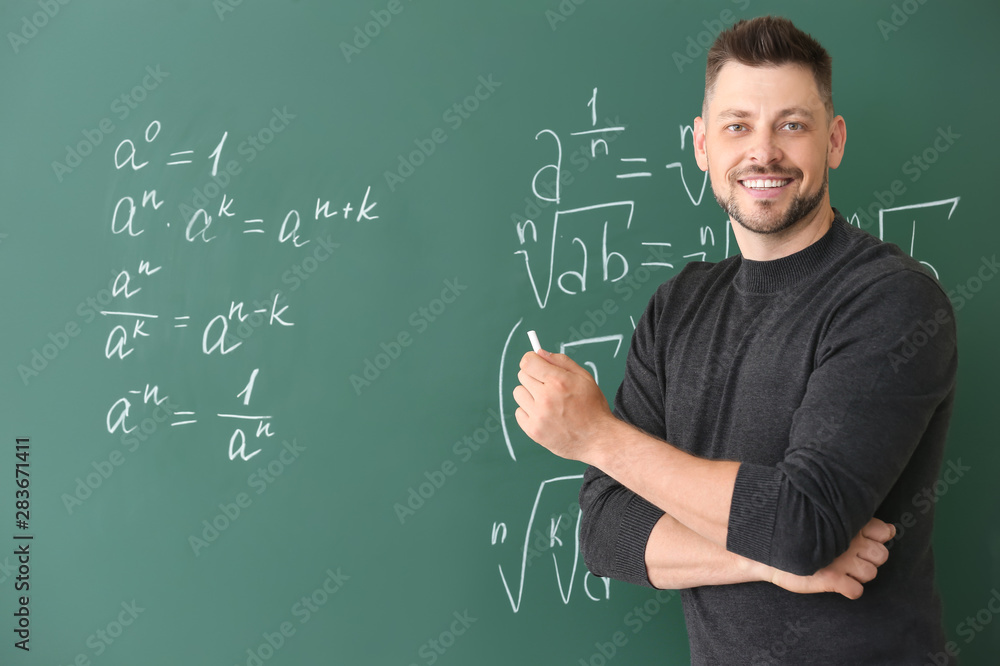 Handsome math teacher writing on blackboard in classroom - obrazy, fototapety, plakaty 