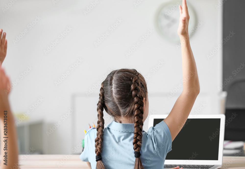 Cute little girl raising hand in classroom