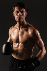 Poster - Concentrated strong handsome young sportsman boxer in gloves posing isolated over black wall background.