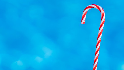 red candy cane on blue water background. New Year and Christmas on pool. Christmas moody background. Copy space. New Year in summer.