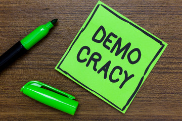 Conceptual hand writing showing Demo Cracy. Business photo showcasing freedom of the people to express their feelings and beliefs Green Paper Communicate ideas Marker Wooden background