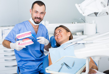 Dentist in uniform with maket of jaw is telling about healthcare