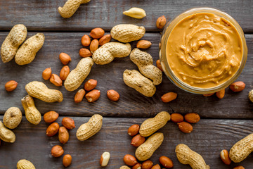 Wall Mural - Product for hearty breakfast with peanut butter in bowl near nuts on wooden background top view pattern