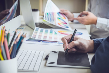 Two colleague creative graphic designer working on color selection and color swatches, drawing on graphics tablet at workplace with work tools and accessories