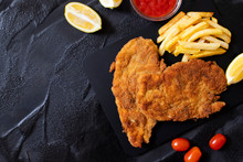 Traditional Chicken Schnitzel Served With French Fries, Sauce And Lemon. Black Background. Top View