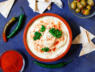 Wall Mural - Healthy homemade hummus served with paprika powder, pita bread, olives and parsley. Middle Eastern cuisine, Israeli cuisine, Levanese cuisine, Levantine cuisine. Dark background. Top view