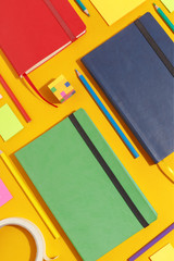 Composition of several stationery notebooks of different colors and stationery on a yellow background. Creative concept of stationery and school supplies. Top view