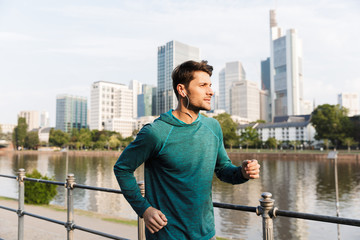 Sticker - Photo of calm serious man listening music with earphones while running near city promenade