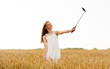 © Syda Productions - technology, summer and people concept - happy young girl in white dress taking picture by smartphone on selfie stick on cereal field
