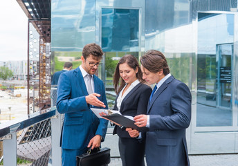 Confident businesspersons talking in front of modern office building. Businessmen and businesswoman have business conversation. Banking and financial market concept.