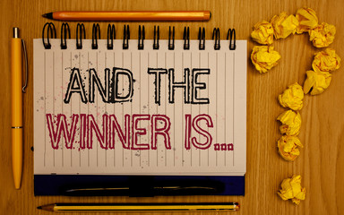 Text sign showing And The Winner Is . Conceptual photo Announcing as first place in competition or race Notepad with outline text pen pencil woody desk crimp balls form query mark