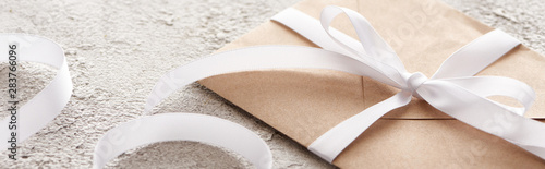 Fotomural panoramic shot of beige envelope with white ribbon on textured surface