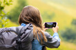 © Андрей Репетий - A girl hiker with cell phone and backpack taking picture of beautiful valley in the mountains. Travel concept.