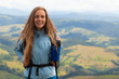 © Андрей Репетий - Hiking. Woman hiker smiling standing outside at the top of a hill with backpack. Outdoor portrait of happy beautiful young woman.