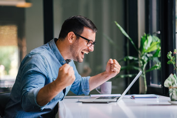 Overwhelmed by success young cheerful adult casual businessman or entrepreneur smiling and vividly celebrating with raised hands and strong voice successful news email or business deal