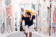 © Emanuele - Smiling man carrying woman on back up steep street, Lisbon