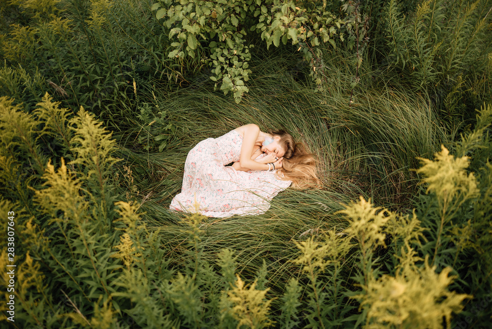 beautiful slender girl with long blonde hair in delicate dress, cute woman lies on the grass from above, fairy-tale princess in the spring garden, gentle image of the queen, fairy in love