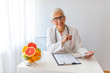 © Dragana Gordic - Female nutritionist sitting at table with clipboard and healthy products on white background. Confident nutritionist working at desk with fresh fruit. Nutritionist doctor writing diet plan on table
