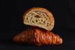 A croissant cut in half on top of a full croissant on black background
