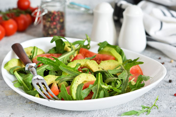 Salad with rucolla, tomatoes, avocado and sauce on the kitchen table. The view is close.