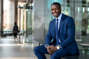 Handsome and stylish modern african american business man entrepreneur executive, sitting outside of office with cheerful smile