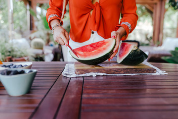 Wall Mural - young woman preparing a healthy recipe of diverse fruits, watermelon, orange and blackberries. Using a mixer. Homemade, indoors, healthy lifestyle