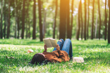 A Beautiful Asian Woman Lying And Reading A Book In The Park
