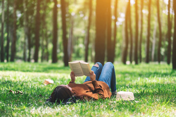 a beautiful asian woman lying and reading a book in the park