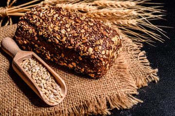 Fresh fragrant bread with grains and cones of wheat against a dark background. Assortment of baked bread on wooden table background. Fresh fragrant bread on the table. Food concept. 