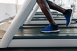 © twinsterphoto - Side view of African American sportsman in blue sneakers working out on electric treadmill in fitness club. Faceless male runner running on treadmill