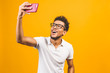 © denis_vermenko - Image of happy young african american man posing isolated over yellow background take a selfie by phone.