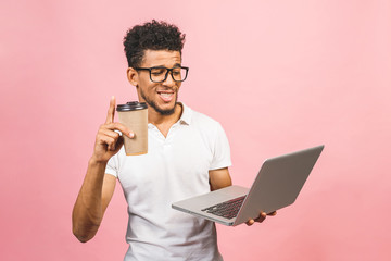 Using laptop. Portrait of handsome casual african american young man drinking coffee while holding laptop computer isolated against pink background.