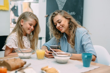 mother and daughter using smartphone while having breakfast