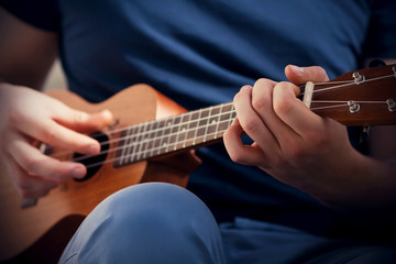 A guy dressed in a dark blue t-shirt and light blue pants plays a cheerful tune on the ukulele