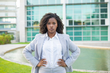 Confident determined businesswoman posing outside. Young black woman wearing formal suit, standing near office building and looking at camera. Confident professional concept