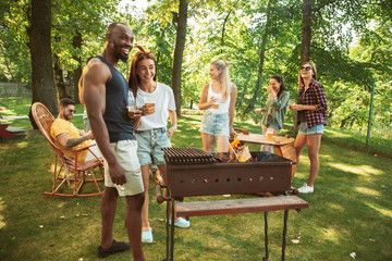 Wall Mural - Group of happy friends having beer and barbecue party at sunny day. Resting together outdoor in a forest glade or backyard. Celebrating and relaxing, laughting. Summer lifestyle, friendship concept.