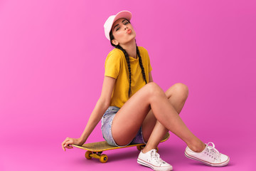 Wall Mural - Image of seductive happy woman wearing casual clothes making kiss face and sitting on skateboard