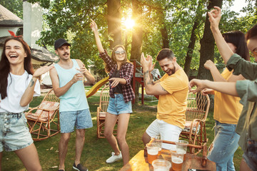 Group of happy friends having beer and barbecue party at sunny day. Resting together outdoor in a forest glade or backyard. Celebrating and relaxing, laughting. Summer lifestyle, friendship concept.