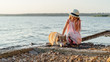 Little beautiful girl in pink dress and hat are playing with siberian husky dog near the sea. young girl are walking on the coast, at the sunset time.