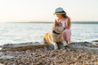 Little beautiful girl in pink dress and hat are playing with siberian husky dog near the sea. young girl are walking on the coast, at the sunset time.