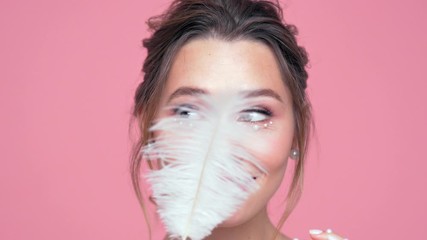 Poster - Close up view of Beauty playful brunette woman with pearls on face and hands posing with peather over pink background