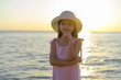 Pretty little girl's back with long beautiful hair in a straw hat and a pink dress in a summer beach. Sunny day, sunset.