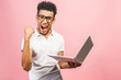 © denis_vermenko - Happy winner! Portrait of happy young afroamerican man using laptop comruter and checkin isolated against pink, celebration